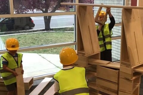 Children wearing vests and hard hats build with large wooden blocks