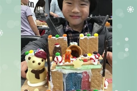 Boy smiling with small structure made of graham crackers, frosting, and candies